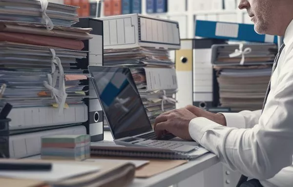 business person at laptop surrounded by papers and files